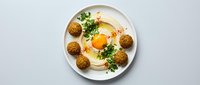 Creamy hummus topped with fresh herbs and spices served with crispy falafel balls on white plate, healthy Mediterranean vegetarian meal from above.
