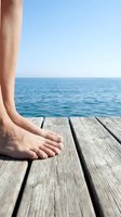 Barefoot person standing on wooden dock overlooking calm ocean waters on clear day. Relaxation and summer vacation concept for travel and leisure lifestyle imagery.