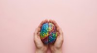 Hands protecting colorful brain model representing mental health awareness, psychology, neuroscience and cognitive wellness on pink background.