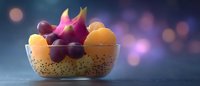 Fresh tropical fruits in glass bowl with dragon fruit, oranges and grapes on dark background with bokeh lights and copy space for food photography.