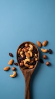 Mixed nuts and dried fruits in wooden spoon on blue background. Healthy snacking, trail mix with almonds, cashews, hazelnuts and raisins for nutrition.