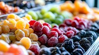 Colorful assortment of frozen berries and fruits arranged in rows including raspberries, blackberries, and yellow cloudberries, creating vibrant pattern of fresh frozen produce.