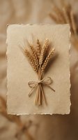 Golden wheat bundle tied with twine on handmade paper creates rustic harvest decoration for autumn crafts and natural design projects.