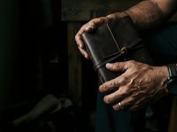 Close-up of mature man's weathered hands holding worn leather journal or notebook, suitable for editorial, lifestyle, and business content.