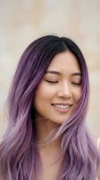 Young Asian woman with long purple ombre hair smiling serenely with closed eyes, natural makeup, soft bokeh background, beauty and hair color concept.