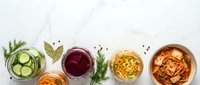 Assorted fermented vegetables in jars and bowls on white marble, top view with copy space. Kimchi, pickled cucumbers, beets, carrots for healthy gut nutrition.