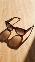 Tortoiseshell sunglasses with dark lenses casting shadows on sandy beige textured surface, ideal for fashion, summer, and lifestyle design projects.
