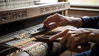 Skilled artisan hands weaving colorful threads on traditional wooden loom creating intricate textile patterns in workshop setting for handmade fabric production.