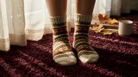 Cozy knitted wool socks with colorful patterns on feet standing on burgundy carpet in warm home interior for comfort and relaxation concepts.