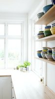Bright Scandinavian kitchen with open wooden shelves displaying colorful ceramic bowls, fresh herbs on windowsill, natural light, minimalist interior.