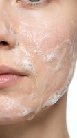 Close-up of a woman's face with exfoliating scrub or mask applied to skin, showing skincare treatment and facial cleansing routine for beauty and wellness purposes.