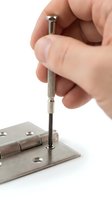 Hand using a small precision screwdriver to tighten a screw on a metal door hinge, close-up repair and home improvement concept.