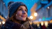 Young woman in knitted hat smiling during snowfall with city lights bokeh in background, creating magical winter atmosphere.