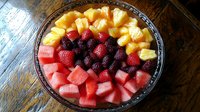 Fresh summer fruit platter with juicy watermelon cubes, sweet pineapple chunks, ripe blackberries and red strawberries arranged in glass bowl on wooden table.