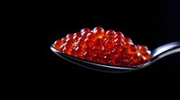 Fresh red caviar on silver spoon against dark background, macro shot showing detailed texture of salmon roe pearls with natural gloss and transparency.