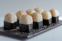 Fresh scallop nigiri sushi rolls arranged on dark plate with sesame seeds, close up view of Japanese cuisine served at restaurant or sushi bar.