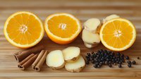 Fresh orange slices with ginger root, cinnamon sticks and black peppercorns arranged on wooden cutting board, natural ingredients for winter drinks.