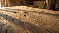 Weathered wooden plank surface with natural grain texture and cracks, rustic barn interior background for carpentry and construction projects.