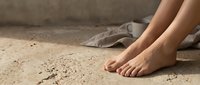 Bare female feet resting on sandy textured ground with soft natural light and linen fabric in background, copy space.