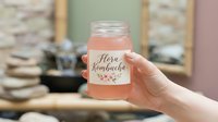 Caucasian woman's hand holding a mason jar with pink kombucha drink and floral label, natural fermented beverage concept.