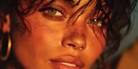 Young woman with curly hair and golden skin in warm sunlight creating dramatic shadows and highlights on face for beauty and lifestyle concepts.