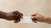 Two hands of different ethnicities exchanging a blank white card against a neutral beige background, representing business communication, partnership, networking, or professional contact sharing.
