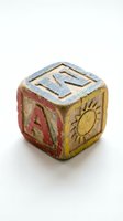 Vintage wooden alphabet block with weathered paint showing letters and sun symbol isolated on white background for nostalgic childhood designs.
