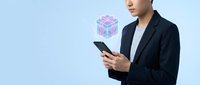Young professional man in dark blazer holding smartphone with holographic cube interface floating above device on light blue background.
