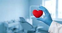 Medical professional in blue gloves holding red heart in modern hospital room. Healthcare, cardiology, heart disease prevention and treatment concept.