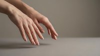Elegant female hands with natural nude manicure gracefully posed on a neutral gray surface, showcasing smooth skin and delicate fingers in soft studio light.