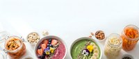 Colorful smoothie bowls with fresh berries, nuts and seeds arranged on white marble surface for healthy breakfast meal prep and nutrition content.