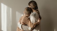 Young Caucasian mother with braided hair embracing her small son in warm natural light creating tender family bonding moment for parenting content.