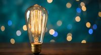 Vintage Edison bulb glowing with warm filament against blurred bokeh lights background. Retro lighting concept for creative projects and design work.