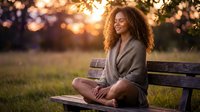 Young African American woman with curly hair meditating peacefully on wooden bench during golden hour sunset, practicing mindfulness and wellness in serene park setting.