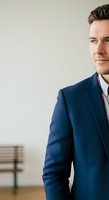 Confident male professional in navy blazer and white shirt with red striped tie, standing against neutral background with bench, suitable for corporate, business, and leadership concepts.