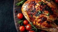 Juicy roasted chicken breast with crispy grilled skin, seasoned with herbs and spices, served with fresh cherry tomatoes and rosemary sprigs on dark background.