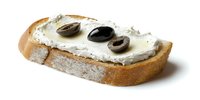 Rustic bread slice with creamy cheese spread topped with black olives on white background, perfect for food menu or culinary blog.
