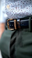 Stylish leather belt with gold buckle detail against polka dot shirt and green pants, showcasing elegant menswear accessories in macro photography.