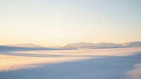 Serene winter beach landscape with snow-covered sand and gentle waves under soft pastel sunrise sky creating peaceful coastal scenery for relaxation themes.