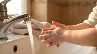 Child washing hands with soap and water at bathroom sink for hygiene and health care routine.