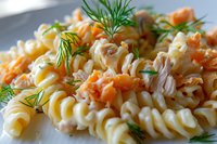 Creamy fusilli pasta with smoked salmon pieces and fresh dill garnish in white sauce, close-up macro shot showing texture and garnish details.