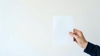 Hand holding blank white card or paper against neutral background for business messaging and branding purposes.