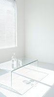 Minimalist interior with glass table, clear water pitcher and drinking glasses, bright natural light streaming through horizontal window blinds creating striped shadows on white walls and floor.
