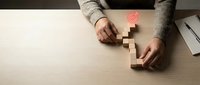 Woman in beige sweater arranging wooden blocks on white desk, demonstrating business strategy, risk management, and problem-solving concepts for corporate training and development materials.