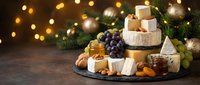 Festive cheese board with assorted cheeses, grapes, walnuts, and honey on slate, decorated with Christmas tree and golden bokeh lights.