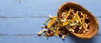 Wooden bowl filled with colorful pasta varieties spilling onto rustic blue wooden background for culinary and cooking projects.