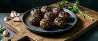 Herb-crusted meatballs with sesame seeds on dark plate, rustic wooden board with garlic and rosemary garnish for gourmet cooking and dining concepts.