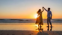 Romantic couple dancing on beach at sunset with golden sky and ocean waves creating silhouettes for love and relationship concepts.