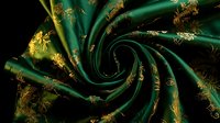 Luxurious emerald green silk fabric with golden floral embroidery swirled in elegant spiral pattern for premium textile and fashion design projects.