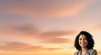 Woman with curly dark hair and olive complexion wearing casual blazer standing outdoors against warm sunset sky with golden and pink clouds.